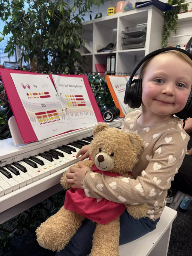 A young child wearing headphones at a colour-coded piano